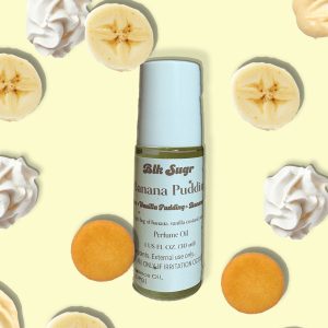 A bottle of Blk Sugr “Banana Pudding” perfume oil on a light yellow background, surrounded by banana slices, whipped cream, vanilla pudding, and vanilla wafer cookies. The label includes notes of banana, vanilla pudding, and custard.