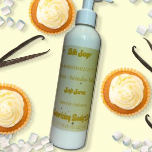 A bottle of Blk Sugr Lemon Marshmallow Cupcake Soft Serve Lotion on a pastel yellow background with lemon cupcakes, mini marshmallows, and vanilla bean pods.