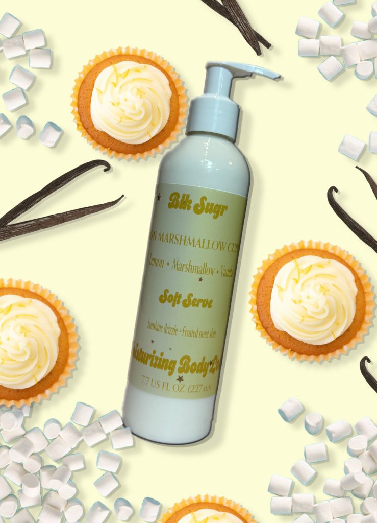 A bottle of Blk Sugr Lemon Marshmallow Cupcake Soft Serve Lotion on a pastel yellow background with lemon cupcakes, mini marshmallows, and vanilla bean pods.