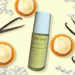 A bottle of Blk Sugr “Marshmallow” perfume oil on a pale yellow background, surrounded by lemon cupcakes, mini marshmallows, and vanilla bean pods. The label includes notes of lemon, marshmallow, and vanilla.