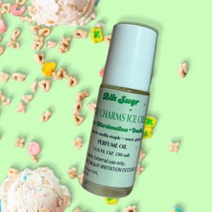 A bottle of Blk Sugr “Lucky Charms Ice Cream” perfume oil on a mint green background, surrounded by scoops of ice cream and colorful cereal pieces resembling marshmallow shapes. The label includes notes of cereal, marshmallow, and vanilla maple.