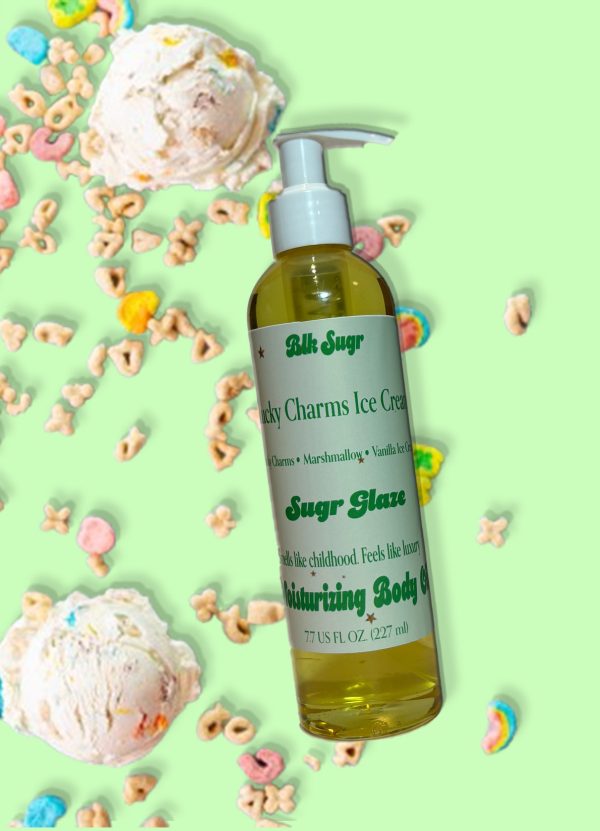 A bottle of Blk Sugr “Lucky Charms Ice Cream” Sugr Glaze body oil on a light green background, surrounded by colorful cereal pieces and scoops of marshmallow ice cream. The label includes notes of Lucky Charms, marshmallow, and vanilla ice cream.