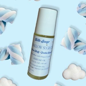 A bottle of Blk Sugr “Mallow Sugr Cloud” perfume oil on a baby blue background, surrounded by twisted marshmallows and fluffy white clouds. The label highlights marshmallow fluff, tonka bean, and whipped vanilla notes.