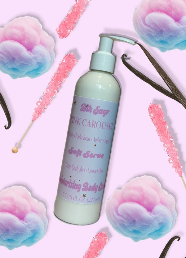 A bottle of Blk Sugr Pink Carousel Soft Serve Lotion on a pastel pink background with cotton candy, pink rock candy sticks, vanilla bean pods, and sugar crystals.