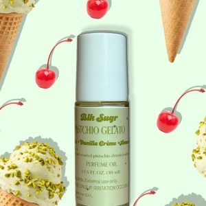 A bottle of Blk Sugr “Pistachio Gelato” perfume oil on a pale mint green background, surrounded by pistachio ice cream cones and red maraschino cherries. The label highlights pistachio, vanilla crème, and amaretto notes.