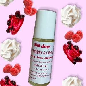 A bottle of Blk Sugr “Raspberry & Crème” perfume oil on a pastel pink background, surrounded by whipped cream, fresh raspberries, and raspberry drizzle. The label highlights notes of raspberry, crème, marshmallow, and vanilla fluff.