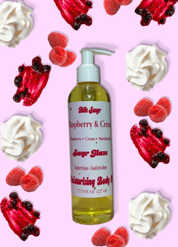 A bottle of Blk Sugr “Raspberry & Creme” Sugr Glaze body oil on a pink background, surrounded by whipped cream, raspberries, and berry sauce drizzle.