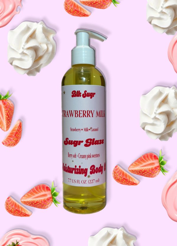 A bottle of Blk Sugr “Strawberry Milk” Sugr Glaze body oil on a light pink background, surrounded by fresh strawberries, whipped cream, and strawberry milk swirls. The label lists notes of strawberry, milk, and caramel.