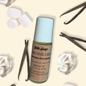A bottle of Blk Sugr “Warm Vanilla Bean” perfume oil on a creamy beige background, surrounded by vanilla beans, whipped cream swirls, and marshmallows. The label notes include vanilla, cashmere woods, and spun sugar.