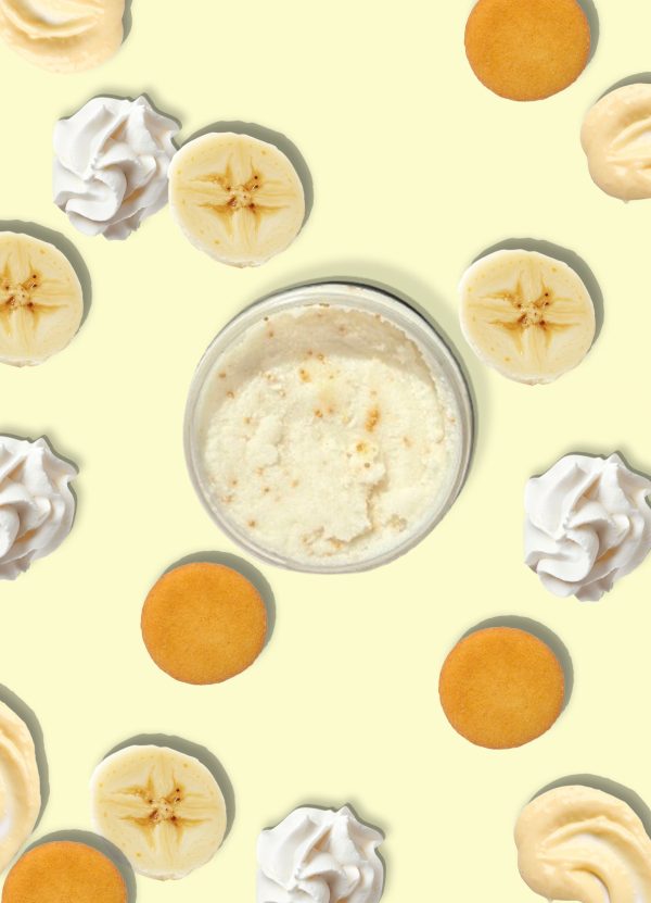 A jar of Blk Sugr Banana Pudding Sugr Buff surrounded by banana slices, vanilla wafers, whipped cream, and banana pudding swirls on a yellow background.