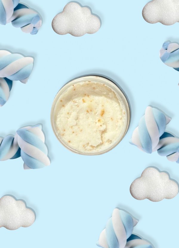 A jar of Blk Sugr Blue Marshmallow Clouds Sugr Buff body scrub on a baby blue background surrounded by fluffy white clouds and twisted blue & white marshmallows.