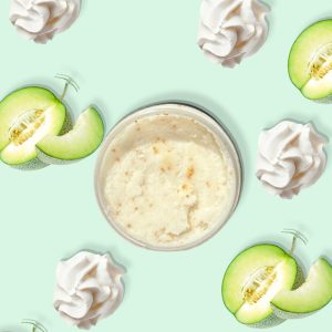 A jar of Blk Sugr Honeydew Whip Sugr Buff surrounded by whipped cream swirls and juicy honeydew melon slices on a mint green background.