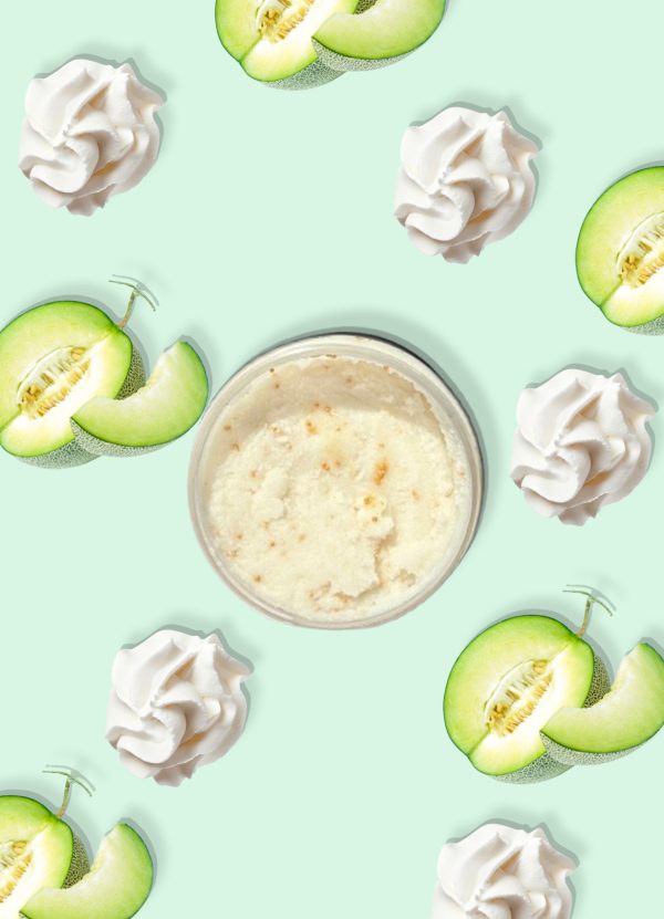 A jar of Blk Sugr Honeydew Whip Sugr Buff surrounded by whipped cream swirls and juicy honeydew melon slices on a mint green background.
