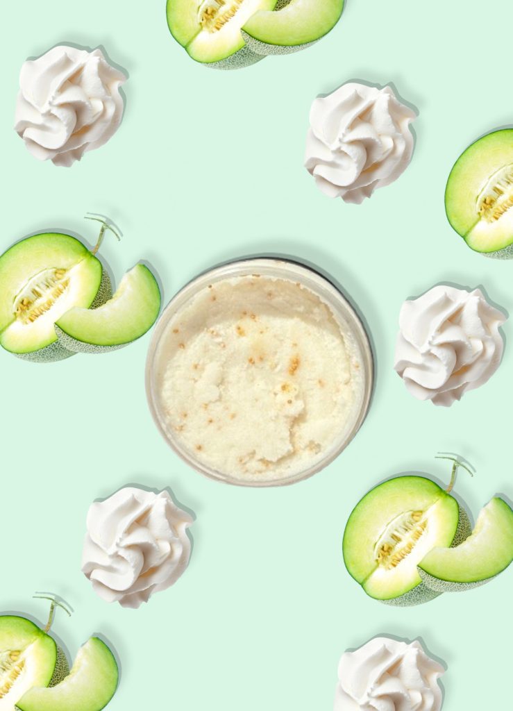 A jar of Blk Sugr Honeydew Whip Sugr Buff surrounded by whipped cream swirls and juicy honeydew melon slices on a mint green background.