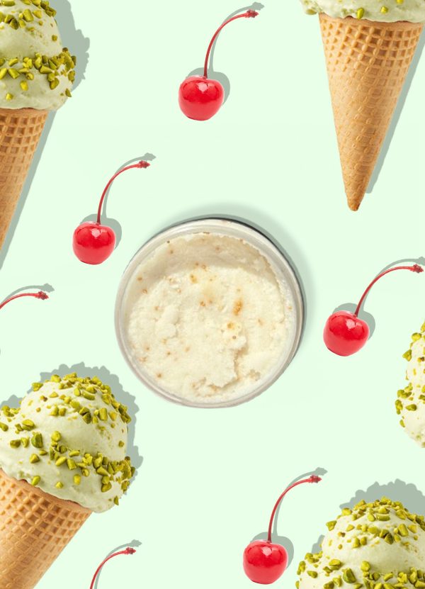 A jar of Blk Sugr Pistachio Gelato Sugr Buff surrounded by pistachio gelato cones and bright red cherries on a mint green background.