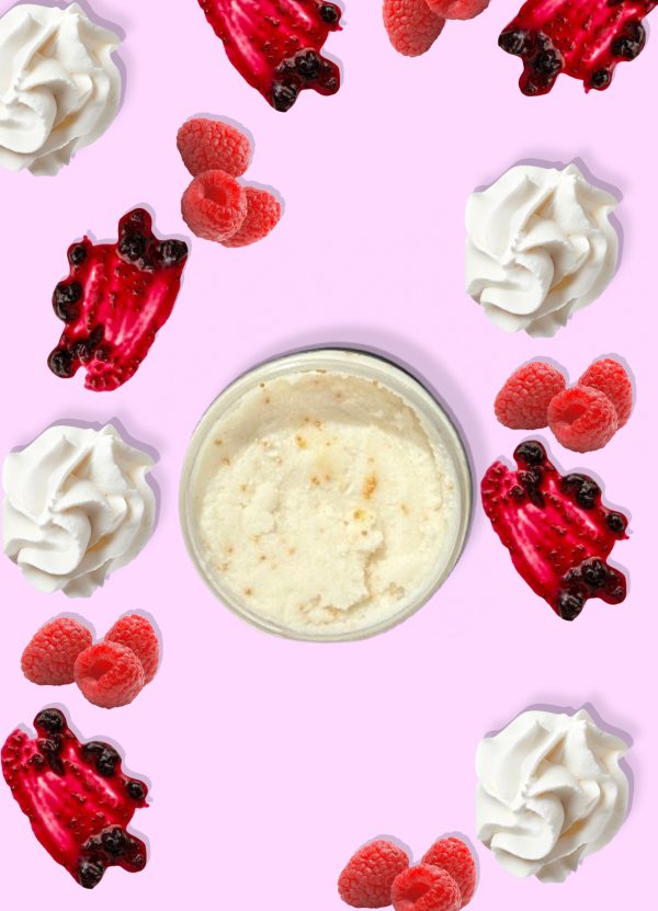 A jar of Blk Sugr Raspberry & Creme Sugr Buff surrounded by raspberries, raspberry jam swirls, and whipped cream on a pink background.