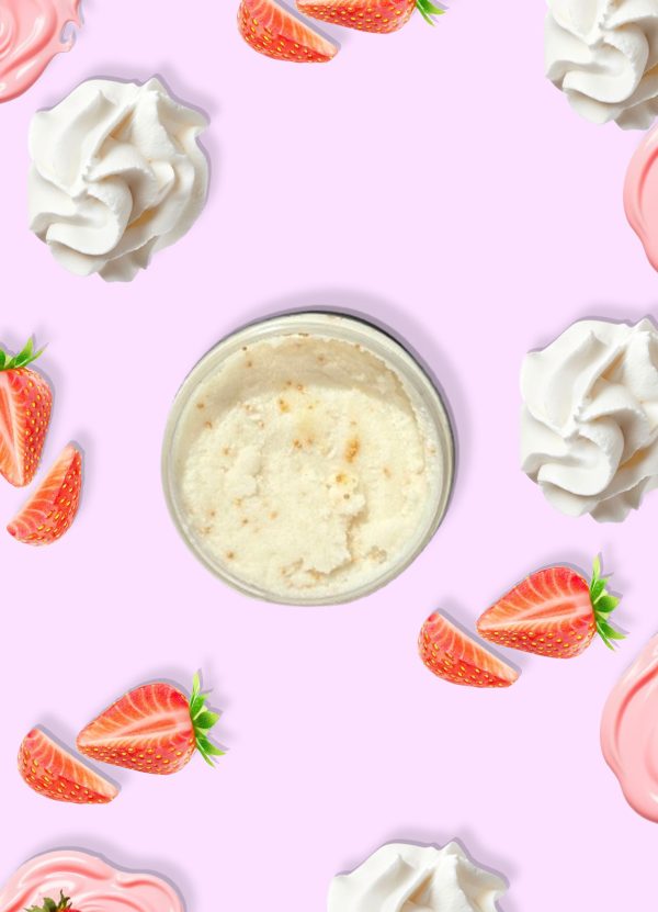 A jar of Blk Sugr Strawberry Milk Sugr Buff surrounded by strawberries, whipped cream, and strawberry frosting swirls on a pink background.