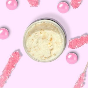 A jar of Blk Sugr Pink Carousel Sugr Buff surrounded by pink rock candy sticks, gumballs, and sugar crystals on a pink background.