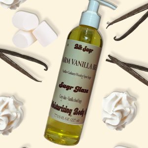 Blk Sugr Warm Vanilla Bean moisturizing body oil with pump, surrounded by whipped cream, vanilla beans, and marshmallows on a cream background.